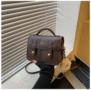 Detail view of a vintage brown crossbody bag with bear embroidery and plush charm