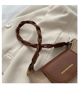 Detail of a beige checkered crossbody bag featuring a brown woven strap and gold metal rings