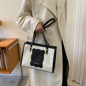 Detail of off-white tote bag with black contrast trim and gold logo lettering on front