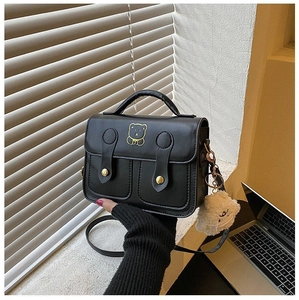 Detail of black leather square handbag featuring golden bear logo and white plush charm