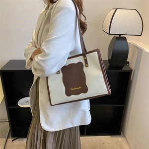 Model wearing a canvas tote bag with brown leather trim and gold logo detail