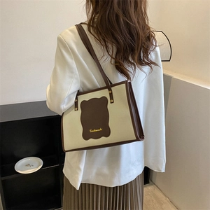 Detail of canvas tote bag with brown leather trim and shoulder strap on model