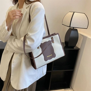 Close-up of cream canvas tote bag with brown leather trim and metallic brand logo