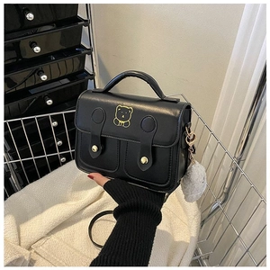 Detail of black crossbody bag featuring gold bear embroidery and white fur ball charm