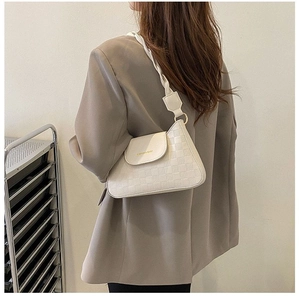 Detail of off-white checkerboard embossed baguette bag with woven shoulder strap