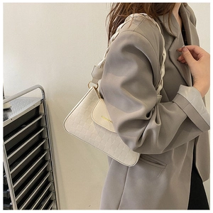 Detail of cream quilted crossbody bag with braided strap and gold hardware on model