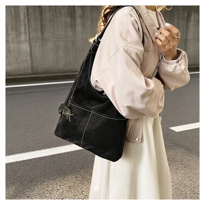 Detail of black tote bag with white contrast stitching and metallic pendant accessory