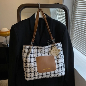 Détail du cabas en tweed à carreaux avec poche en cuir et breloque chat sur un blazer