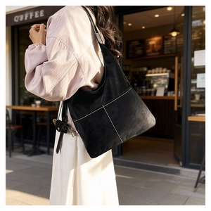 Matte black hobo bag with white stitching detail worn over the shoulder outdoors