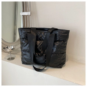 Close-up of black quilted puffer tote bag featuring durable woven straps on white surface