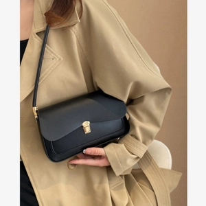 Classic black leather saddle shoulder bag with gold clasp shown on trench coat model
