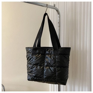 Detail of black quilted puffer tote bag featuring oversized stitching and reinforced straps