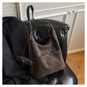 Close-up of brown suede hobo bag with white stitching and mini charm on leather sofa