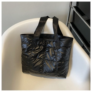 Close-up of black quilted puffer tote bag on a white chair showing glossy nylon texture