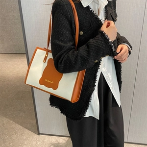 Minimalist creamy white canvas tote bag with brown bear patch and leather shoulder strap
