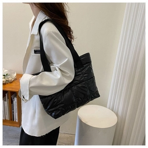 Detail of a black quilted puffer tote bag on shoulder, featuring chic padding and wide straps