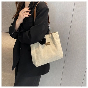 Dettaglio della borsa tote beige trapuntata con ciondolo a pompon e tracolla in pelle