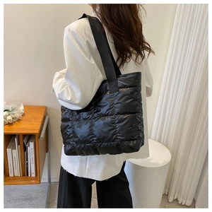 Close-up of black quilted puffer tote bag showing the glossy diamond pattern texture