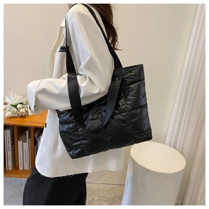 Detail of a black quilted puffer tote bag in glossy nylon worn by a person in white suit