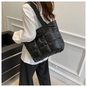 Detail of black quilted puffer tote bag with wide strap worn by a model in a minimal setting