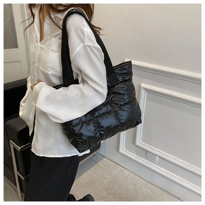 Close-up of black quilted puffer tote bag worn over the shoulder by a model in a minimalist room