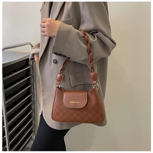 Detail of dark brown embossed shoulder bag with checkered texture and woven strap