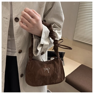 Close-up of brown butterfly buckle underarm bag with pleated strap and bow detail