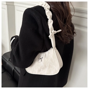 Detail of white pleated shoulder bag with black metal bow and scrunched strap texture
