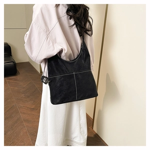 Detail view of the black tote bag featuring contrasting white stitching and a round charm