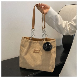 Dettaglio della borsa tote trapuntata marrone con manici a catena e pompon nero