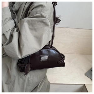 Detail of dark brown leather shoulder bag with silver logo plate on trench coat