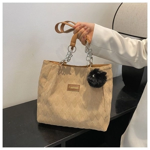 Dettaglio della borsa tote trapuntata beige con manici a catena e ciondolo a pompon nero