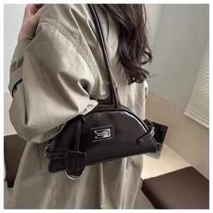 Macro view of a dark brown glossy patent leather shoulder bag with a metal logo plaque