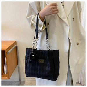 Dettaglio tote bag nera trapuntata con etichetta fashion, catena e ciondolo peluche