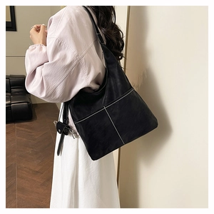 Detail of black matte shoulder bag featuring white contrast stitching and hobo style shape