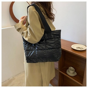 Close-up of black quilted puffer tote bag with wide straps on a trench coat