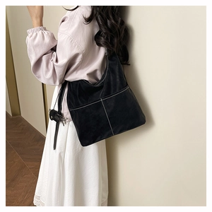 Detail of black crescent shoulder bag with white contrast stitching and mini pouch charm