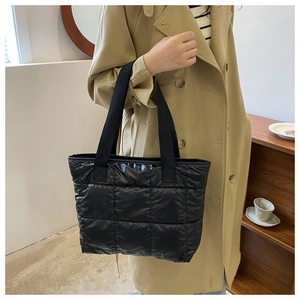 Close-up of black quilted nylon tote bag with puffer texture on a trench coat model