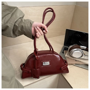 Detail view of burgundy patent leather bag with silver metal plate and long strap