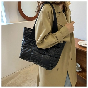 Close-up of a black quilted puffer tote bag worn over the shoulder on a stylish trench coat