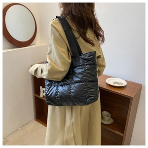 Detailed back view of a black puffer tote bag with quilted padding on model's shoulder