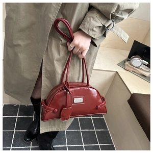 Detail of red patent leather crescent bag with thin double handles and metal plaque