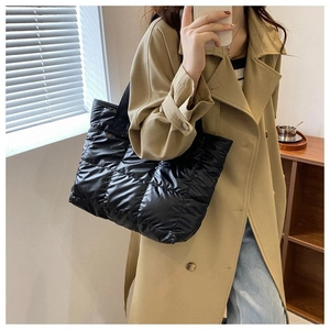 Close-up of a black quilted puffer tote bag on a model wearing a khaki coat