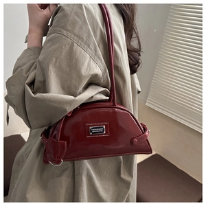 Detail of burgundy patent leather underarm bag with silver plaque on khaki trench coat