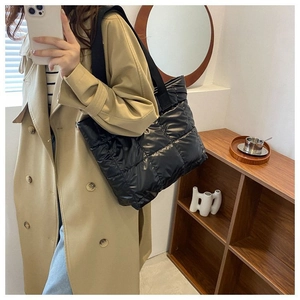 Detail of a black quilted tote bag with a glossy finish and wide fabric shoulder strap
