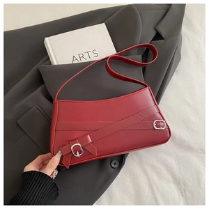 Detail of red matte leather shoulder bag with cross strap design and silver buckles