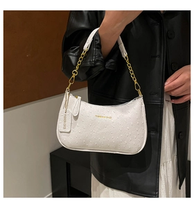 Macro shot of white ostrich pattern leather underarm bag with gold chain strap detail