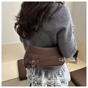 Detail of retro brown underarm bag featuring cross leather straps and bow accent