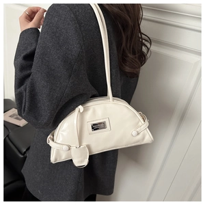 Detailed side view of a cream half-moon underarm bag with glossy finish and metal logo plate