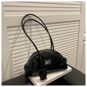 Detail of glossy black moon bag with dual straps resting on a decorative book
